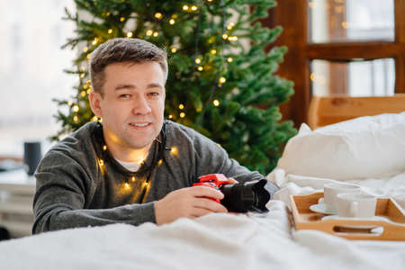 man with camera in red case by bed against background of Christmas decorationsの写真素材