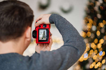 a man takes a picture of a Christmas tree with a red camera.の写真素材