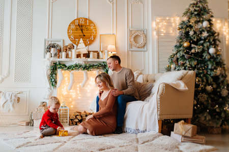 mom and dad give box with a gift to little son in room decorated for new yearの写真素材