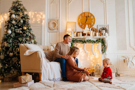 mom and dad give box with a gift to little son in room decorated for new yearの写真素材