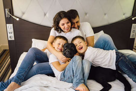 pregnant mother, father and two sons in jeans and white t-shirts on bed.