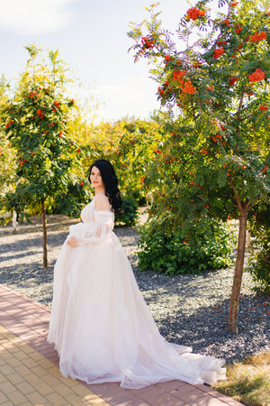 beautiful brunette bride in a wedding dress in a park with rowan trees.の写真素材