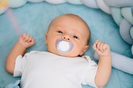 a baby with a pacifier in his mouth lies on a blue diaper.の写真素材