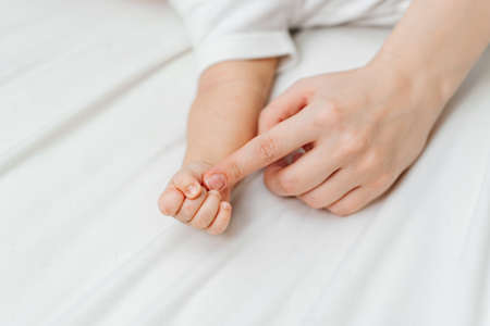 a small babys hand and a mothers hand on a white sheet.