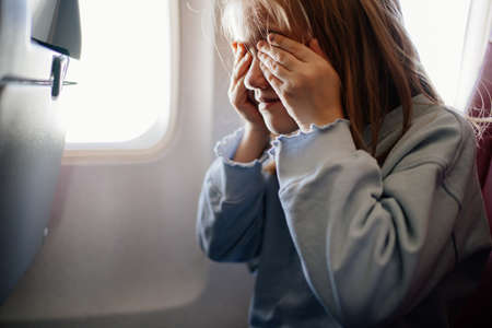 fear of flying. a kid girl closes her eyes with her hands in the airplane seatの写真素材