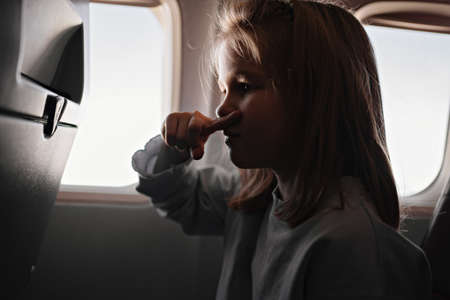 a little girl clamps nose because of unpleasant smell in airplane seat by window