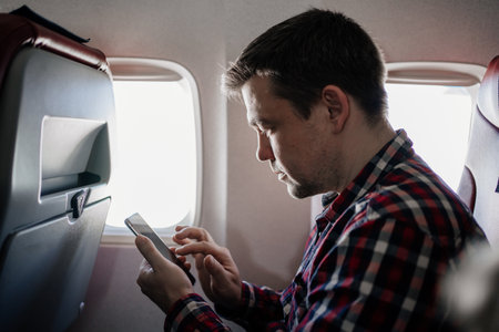 man in plaid shirt sms on phone in seat of passenger on board of plane.の写真素材