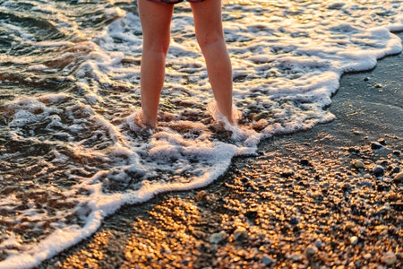 at sunset. legs of girl walking along seashore.の写真素材