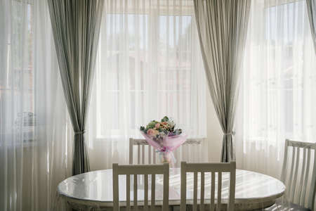 white oval table with a bouquet of flowers in a room with large windows.の写真素材