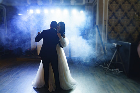 the bride and groom in wedding dresses dance in a dark hall in heavy smoke.の写真素材