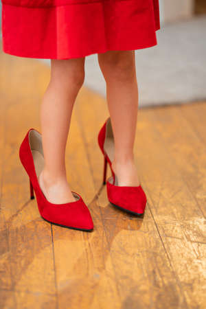 the feet of a little girl in her mothers red heeled shoes.の写真素材