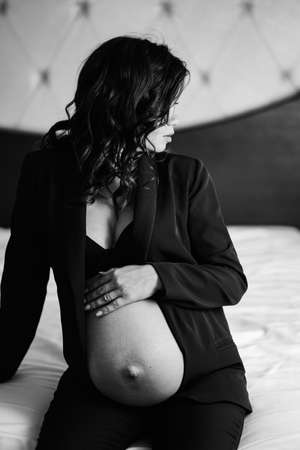 a pregnant woman in a black jacket with bare breasts and a belly on the bed