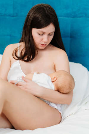 mother in silk nightshirt feeds baby with breast milk in bed. breastfeeding.