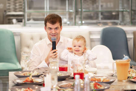 a man with a young son sits at a table and makes a toast into the microphone.の写真素材