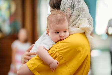 man and woman with baby son in light-colored robes by window in church.
