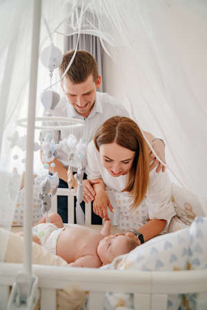 parents near a baby lies in a white crib with canopyの写真素材