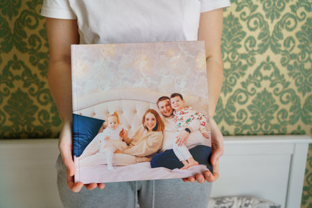 a woman holds a book with photos of big family at homeの写真素材