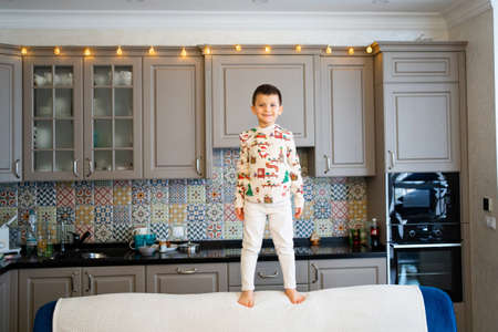 a little boy in pajamas stands on the back of a couch in the dining room.の写真素材