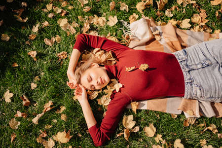 an attractive blonde woman lies on a green lawn with autumn leaves.