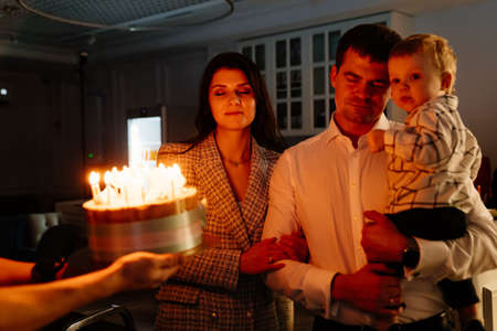 a father and mother with a kid son make a wish and blow out candles on the cake.