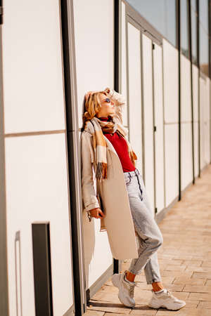 student or businesswoman in sunglasses and a coat with scarf walks down a streetの写真素材