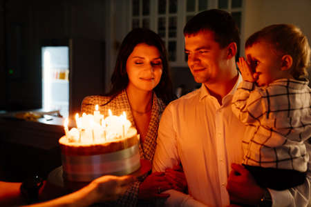 a father and mother with a kid son make a wish and blow out candles on the cake.の写真素材