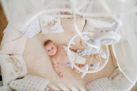 view from above. a baby lies in a white crib with mobile with toys.の写真素材