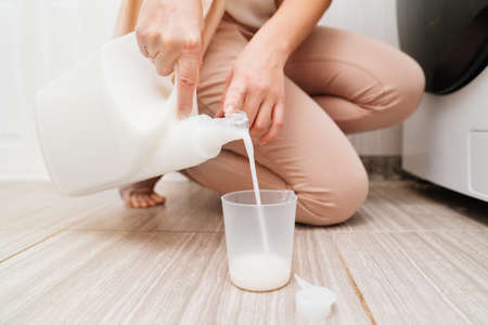 a woman pours laundry detergent for the washing machineの写真素材
