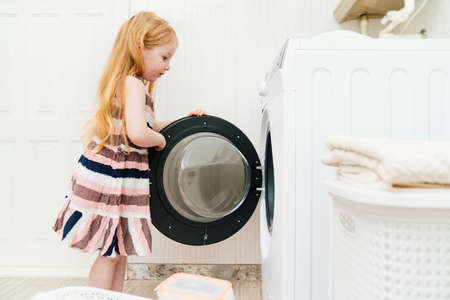 a cute little girl closes or opens the washing machine door.