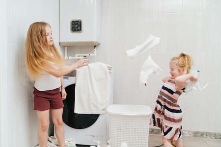 two cute and cheerful girls play with laundry in the laundry room.の写真素材