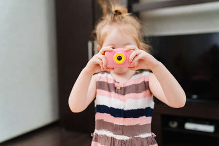 a funny little girl takes a photo on a little pink toy camera.の写真素材