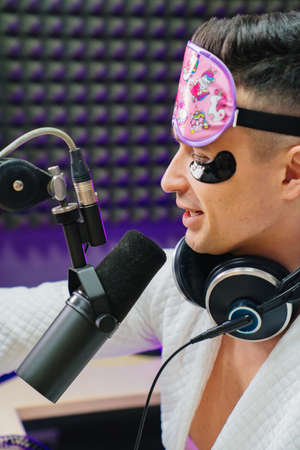A funny radio presenter in a sleep mask, bathrobe and cosmetic patches