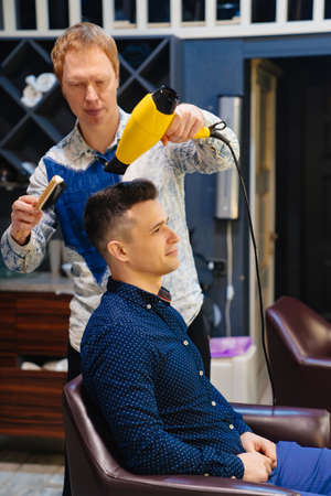 hairdresser dries hair dryer brunette man in a barbershopの写真素材