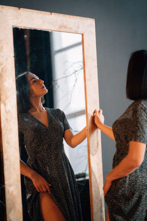 an attractive brunette woman in a black dress by the mirror.の写真素材