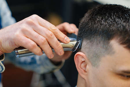 hairdresser makes a haircut of nape for a man with a hair clipper in barbershop