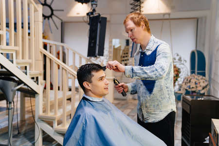 the hairdresser makes a haircut for a man with a hair clipper in a barbershop