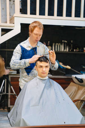 hairdresser makes a haircut for a brunet man with a scissors in a barbershop