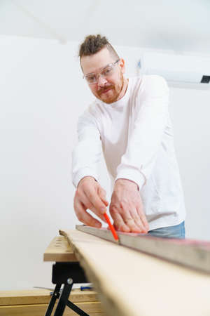 carpenter in protective gloves and glasses makes measurements and draws on wood