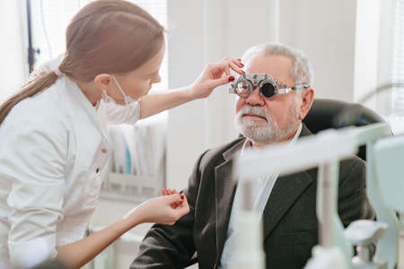 ophthalmologist makes selection of lenses, diagnoses a elderly mans vision.