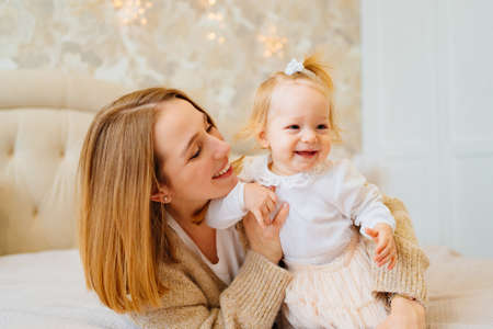 Cute mom and baby daughter lie down, play and hug in bed. games with children.の写真素材