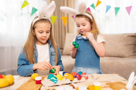 little girls with rabbit ears celebrate Easter and decorate eggs with paintsの写真素材