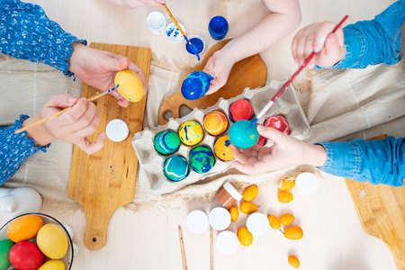 top view. hands of mom and daughters decorate Easter eggs with paints.