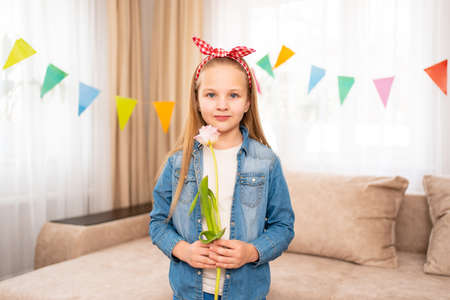 cute and funny little girl with a red headband holds pink tulip flower in handsの写真素材