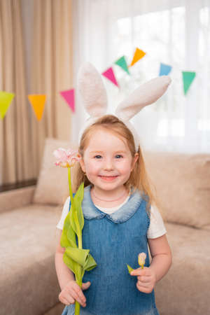 cute and funny little girl with rabbit ears holds pink tulip flower in handsの写真素材