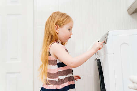 a cute little girl independently turns on the washing machine.の写真素材