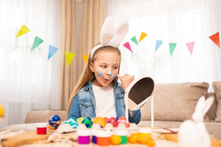 a cute girl looks at the a mirror with a painted face. Easter traditions.