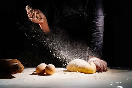 women kneads dough and scatters flour on a black background.