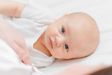 a cute baby with a drop of milk in the corner of mouth on the bed near mother.