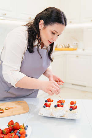 woman cook decorates cakes anna pavlova with strawberries and blueberries