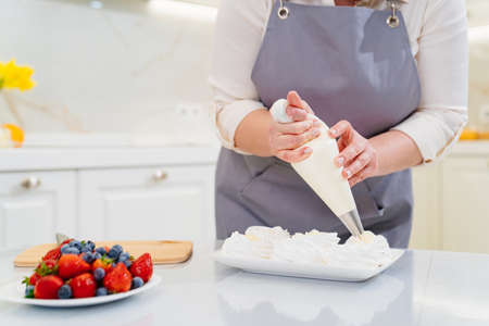a female chef adds cream from a pastry bag to Anna Pavlova cakes in the kitchen.の写真素材